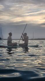 A couple enjoys paddleboarding during sunset, creating a serene and romantic atmosphere on the water.