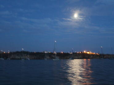 A nighttime view of a harbor with distant lights and a full moon, but the image is unclear and lacks focus.