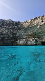 A stunning view of a rocky coastline with a cave entrance, surrounded by crystal-clear turquoise waters — an ideal spot for exploration and adventure.