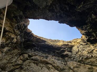 An unclear view from inside a cave looking up towards the sky, showcasing rocky formations. The image lacks identifiable subjects or clarity.
