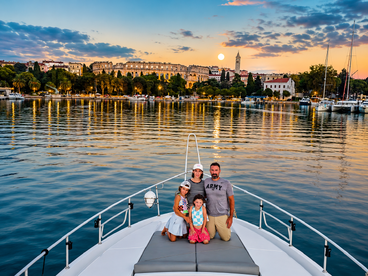 A family poses on the bow of a boat during a stunning sunset, with a picturesque waterfront in the background — a perfect moment for family bonding on the water.