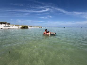 A couple enjoys a refreshing swim in shallow waters at a picturesque sandbar, surrounded by beautiful scenery — perfect for a fun day on the water.