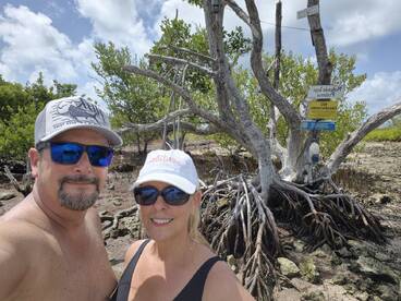 A couple poses for a selfie in front of a mangrove tree, capturing a memorable moment during their outdoor adventure.
