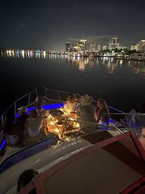 A lively group enjoys a night out on the boat, surrounded by a stunning city skyline and reflections on the water — perfect for dinner cruises and celebrations.