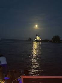 A serene night scene featuring a boat with guests enjoying the moonlight reflecting on the water, creating a picturesque atmosphere perfect for evening cruises.
