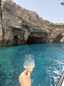A hand holds a glass of champagne against a stunning backdrop of turquoise waters and rocky caves, perfect for celebrating special moments on a boat trip.