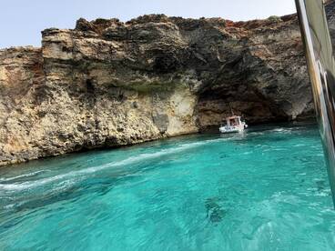A boat navigates through a stunning cave surrounded by crystal-clear turquoise waters, showcasing the beauty of the coastline.