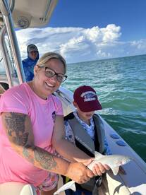 A child and an adult proudly display a caught shark while fishing on a boat, showcasing a memorable family fishing experience.