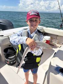 A young boy proudly holds a shark he caught while fishing on a boat, showcasing a memorable moment of wildlife interaction on the water.