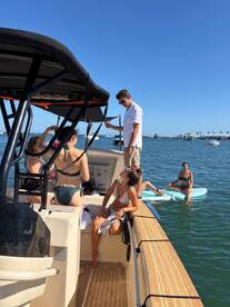 A lively group enjoys a day on the water, with some relaxing on the boat and others paddleboarding nearby — perfect for summer fun and social gatherings.