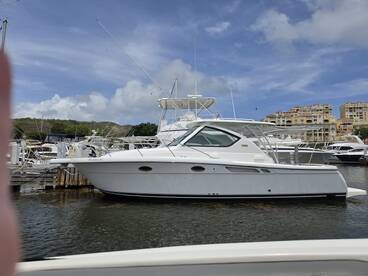 A sleek yacht docked at the marina, showcasing its elegant design against a backdrop of blue skies and nearby buildings.