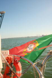 A vibrant view of a Portuguese flag waving on a boat, set against a backdrop of calm waters, perfect for showcasing maritime adventures in Portugal.