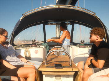Inside view of a sailboat's helm area, featuring guests seated while one person navigates — perfect for showcasing the cozy interior of a sailing experience.