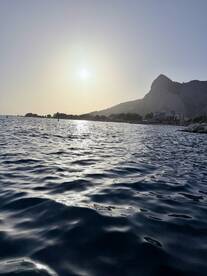 A serene sunset view over the water, with a picturesque coastline and mountains in the background — perfect for capturing the beauty of nature during a boating trip.