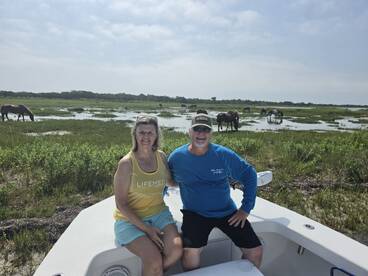 A couple enjoys a scenic boat trip, with wild horses grazing in the background — a perfect blend of nature and adventure.