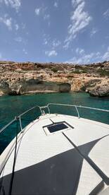 A clear view of the bow of a boat with stunning turquoise waters and rocky cliffs in the background, perfect for showcasing the beauty of a day on the water.