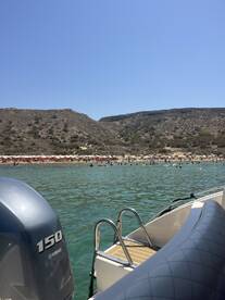 A scenic view from a boat showing a bustling beach with sunbathers and swimmers enjoying the clear waters — a perfect summer getaway.