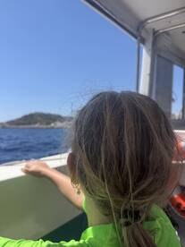 A child enjoys the view from a boat, gazing out at the ocean and nearby island — a perfect moment of adventure on the water.