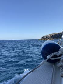 A serene view of a boat's hull against the backdrop of a clear blue ocean and rocky coastline, perfect for showcasing the beauty of maritime adventures.