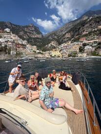A lively group enjoys drinks and sunshine on the deck of a boat, with the stunning coastline of Positano in the background — perfect for memorable boat parties and celebrations.