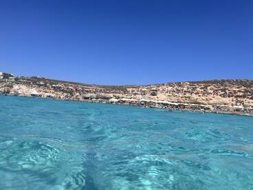 A vibrant scene of a crowded beach with crystal-clear turquoise waters, perfect for swimming and enjoying the sun.