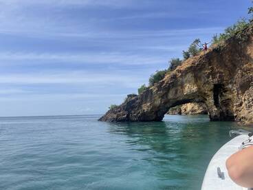 A stunning view of a natural rock arch with a person celebrating on top, showcasing the beauty of the coastline — perfect for adventure seekers exploring the waters.