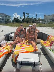 A lively group of friends enjoys a sunny day on a pontoon boat, celebrating with beach vibes and colorful towels — perfect for summer outings and beach parties.