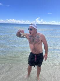 A man excitedly holds up a crab while standing in shallow water, showcasing a fun wildlife encounter during a beach day.