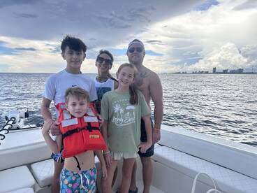 A joyful family poses together on a boat, showcasing their adventure on the ocean, complete with life jackets for safety.