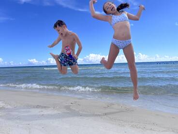 Two kids joyfully jumping on the beach, capturing the essence of summer fun and adventure by the water.