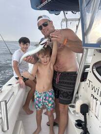 A joyful fishing trip captures a father and his two children proudly displaying their catch aboard a boat — a perfect family bonding experience on the water.