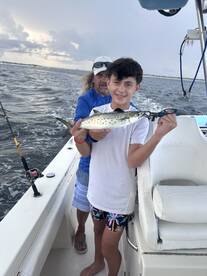 A young boy proudly holds up his catch while fishing on a boat, showcasing a memorable fishing experience with family.