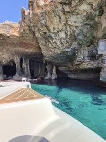 A stunning view of a boat approaching a cave with crystal-clear turquoise waters, showcasing the natural beauty of the coastline.