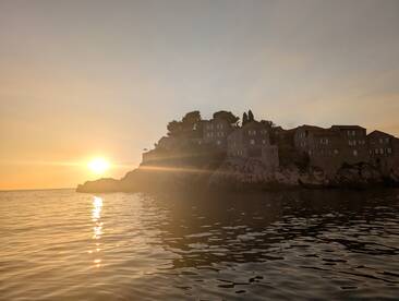 A stunning sunset casts a golden glow over the coastline, highlighting the charming stone houses perched on the cliffside — a picturesque scene perfect for evening boat tours.