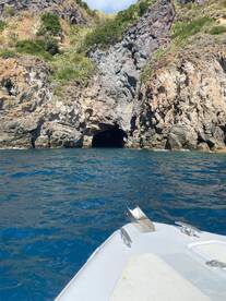A scenic view of a cave entrance along a rugged coastline, captured from the bow of a boat — perfect for exploring hidden gems on the water.