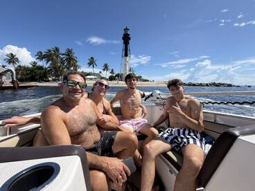 A cheerful group enjoys a sunny day on the boat, with a lighthouse in the background — perfect for family outings and fun on the water.