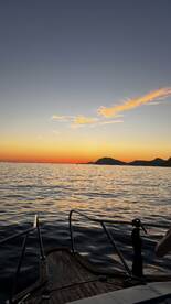 A serene sunset view from the deck of a boat, showcasing the tranquil waters and distant hills — perfect for evening cruises.