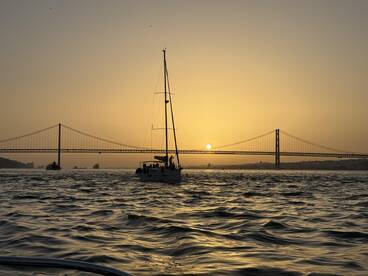 A beautiful sunset view of a sailboat cruising under a bridge, capturing the essence of a serene sailing experience on the water.