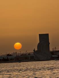 A stunning sunset casts a warm glow over the water, highlighting a prominent landmark in the foreground — a perfect scene for evening boat tours.