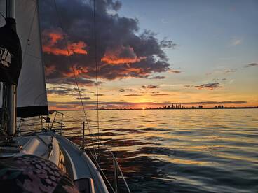 A stunning sunset view from a sailboat, showcasing vibrant colors reflecting on the water with a city skyline in the background — perfect for romantic evening sails or peaceful retreats on the water.