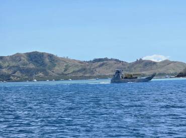 A vessel navigates through clear waters with a scenic backdrop of lush hills, showcasing the beauty of maritime travel.