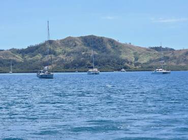 A serene view of multiple sailboats anchored in calm waters, surrounded by lush green hills — a perfect setting for sailing enthusiasts.
