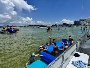 A lively group enjoys a fun day on the water with floating mats, drinks, and camaraderie — perfect for summer parties and water activities.