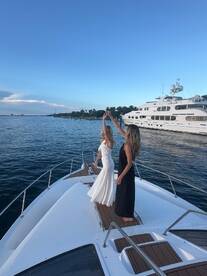 Two women celebrate on the bow of a yacht, dancing joyfully against a stunning waterfront backdrop — perfect for memorable occasions and gatherings on the water.