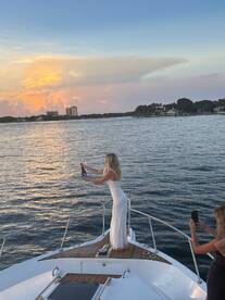 A woman celebrates with champagne on the bow of a yacht at sunset, capturing a perfect moment of joy and elegance on the water.