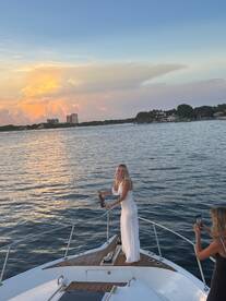 A joyful celebration at sunset aboard a yacht, featuring a woman toasting with champagne while another captures the moment — perfect for memorable gatherings on the water.