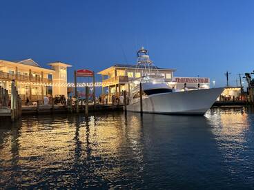 A stunning yacht docked at Fisherman's Wharf, illuminated by evening lights, reflecting beautifully on the water — a perfect setting for fishing enthusiasts and boat lovers.