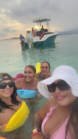 A lively group of friends enjoys a fun day in the water, with a boat in the background and a beautiful sunset setting the scene.