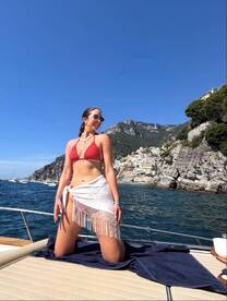 A woman poses on the deck of a yacht against a stunning coastal backdrop, capturing the essence of summer fun and adventure on the water.