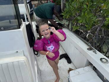 A joyful child in a pink flotation suit smiles while holding a shell on a boat, capturing the essence of fun and adventure on the water.